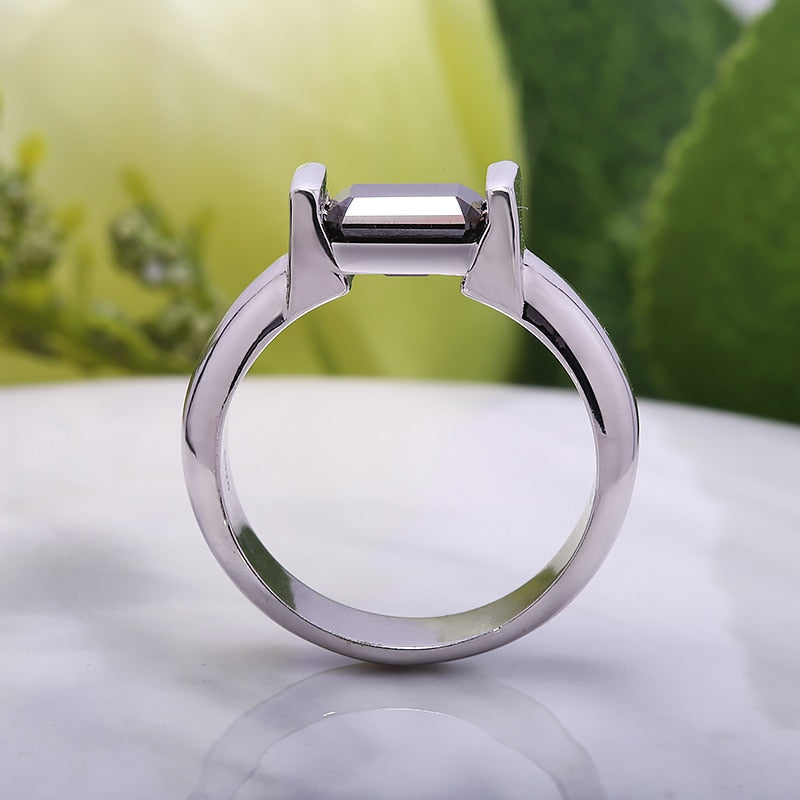 A silver ring with an emerald cut black moissanite side east to west in a tension setting.