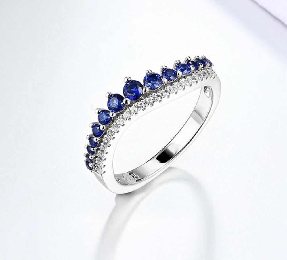 A silver wave design band with varying size blue sapphires and small clear gems below the sapphires.