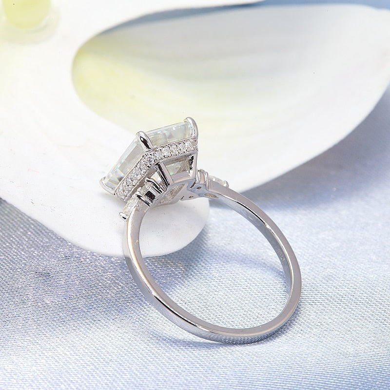 A silver ring with a 5CT emerald cut moissanite set between small round and small pear cut moissanites.