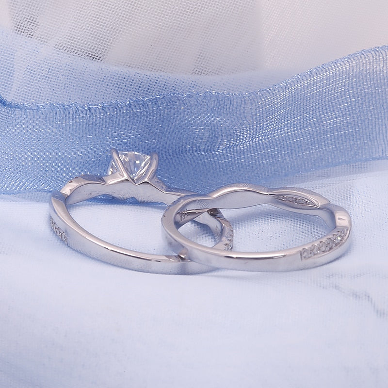A silver engagement ring set with a round moissanite on a half pave twisted shank and a matching wedding ring.