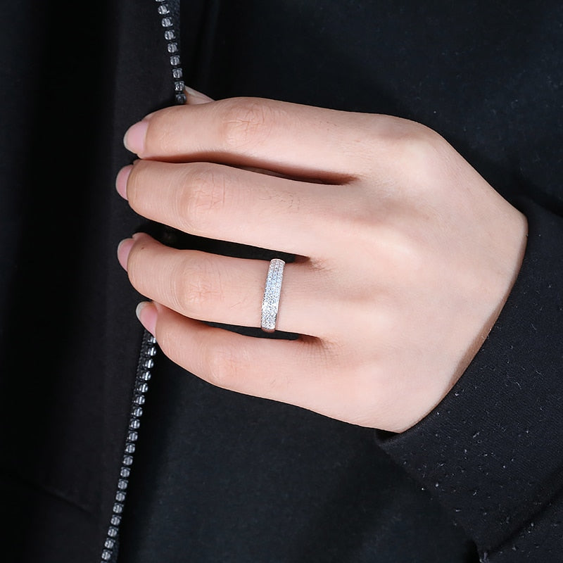 A hand wearing a wide silver wedding band with tiny inset gems.