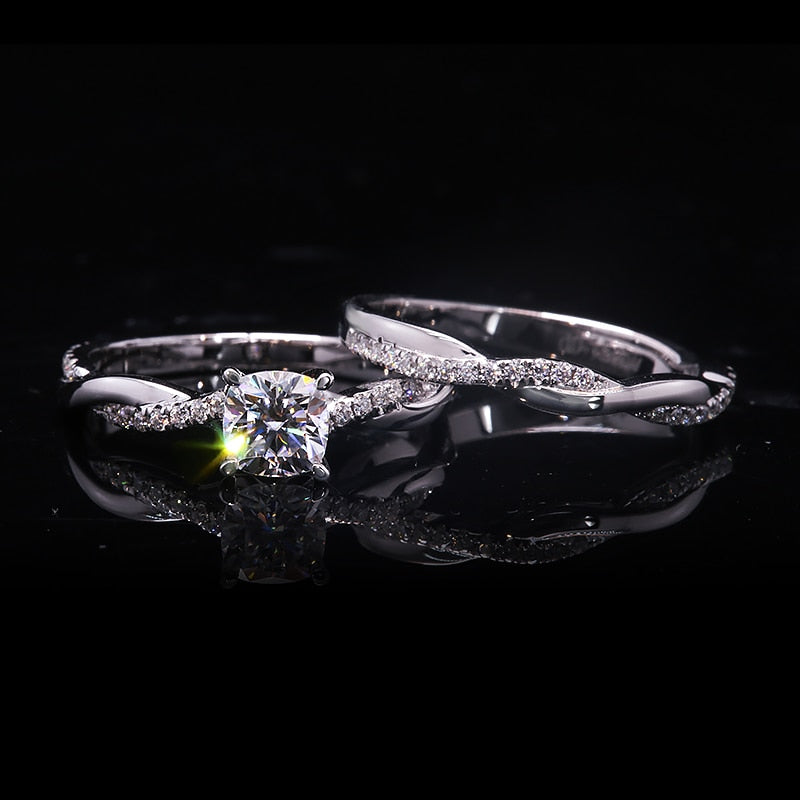 A silver engagement ring set with a round moissanite on a half pave twisted shank and a matching wedding ring.
