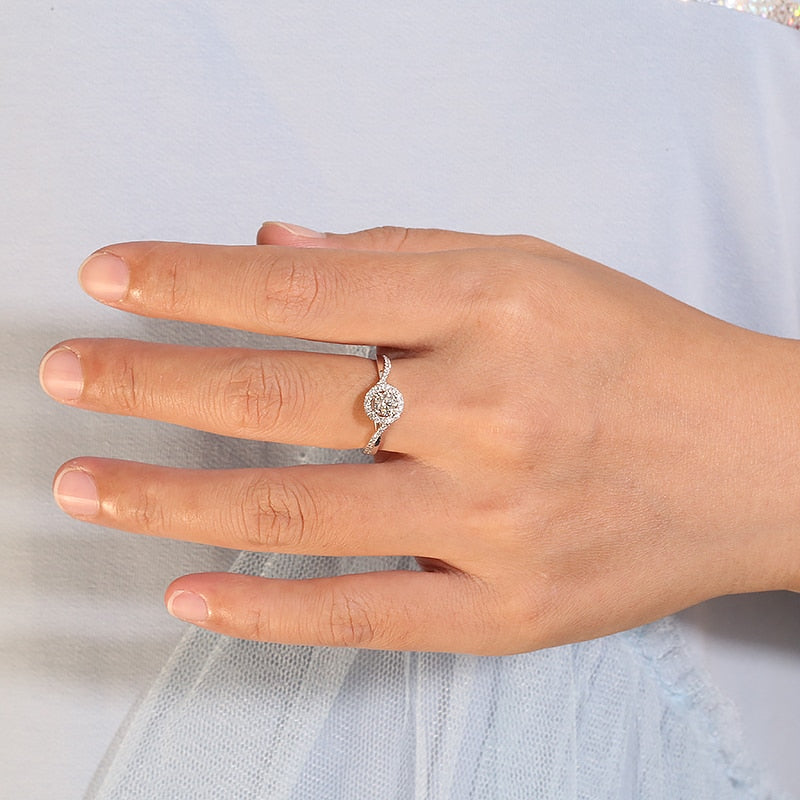 A hand wearing a silver round halo ring with a half pave split shank twisted band.