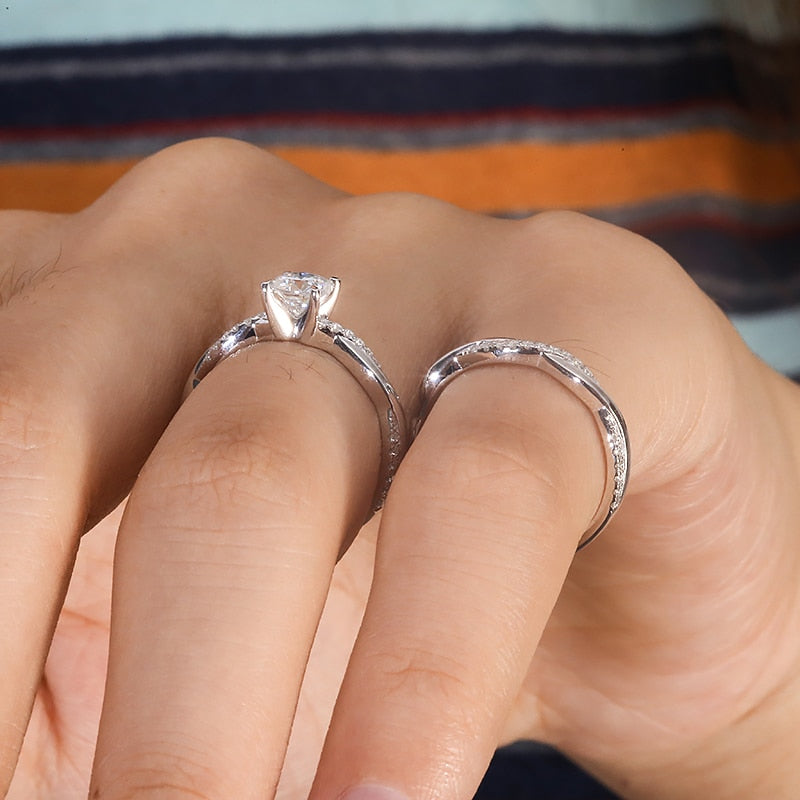 A hand wearing a silver engagement ring set with a round moissanite on a half pave twisted shank and a matching wedding ring.