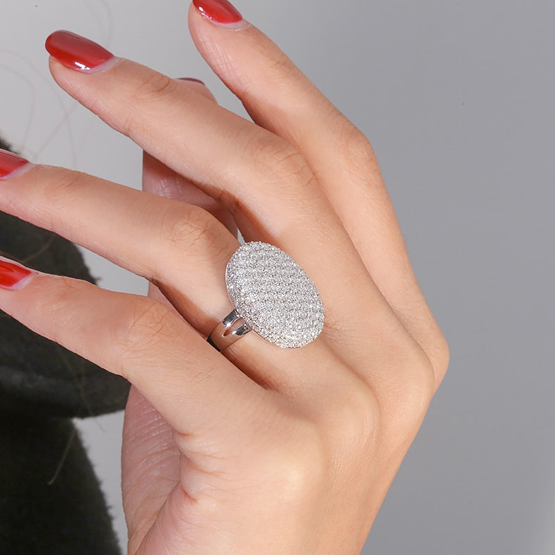A hand wearing a oval shaped silver gem encrusted thick shield style ring.