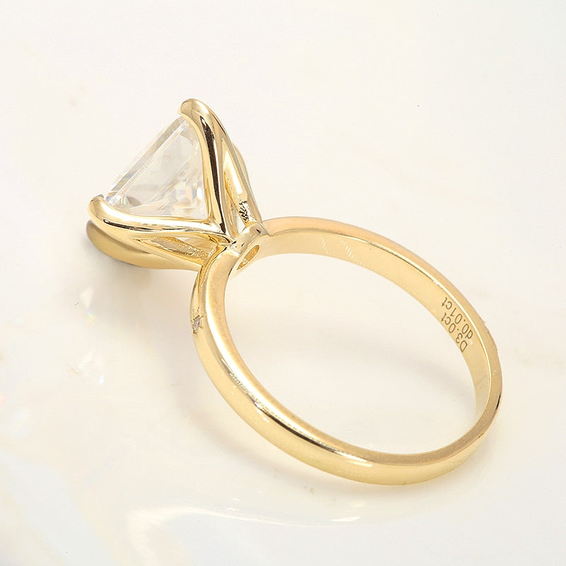 A gold solitaire band petal prong set with a 3CT princess cut moissanite, diagonally set with a tiny moissanite inset on each side of it.