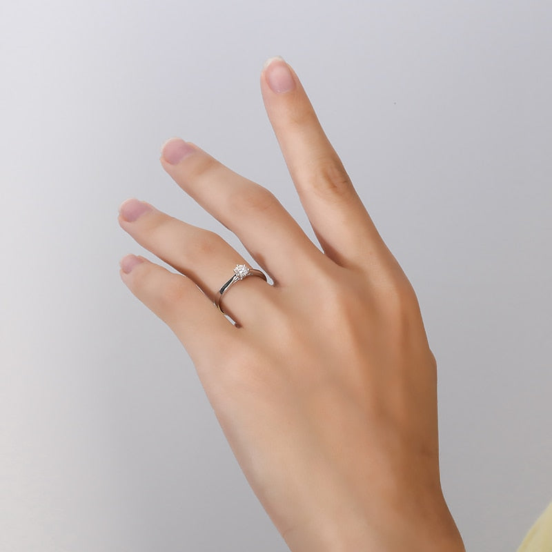 A hand wearing a silver small round solitaire with a tapered band.