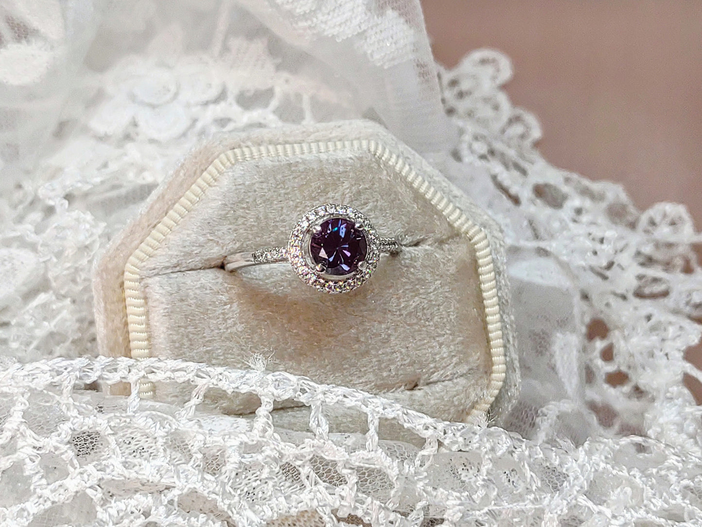 A silver halo ring set with a round dark purple and green lab grown alexandrite gem.