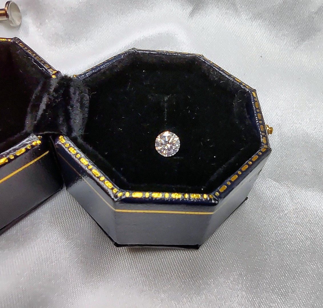 A small brilliant round cut moissanite sitting in an antique style ring box.