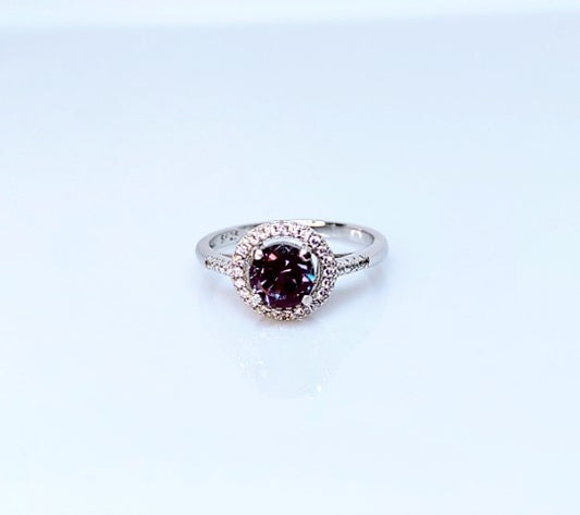 A silver halo ring set with a round dark purple and green lab grown alexandrite gem.
