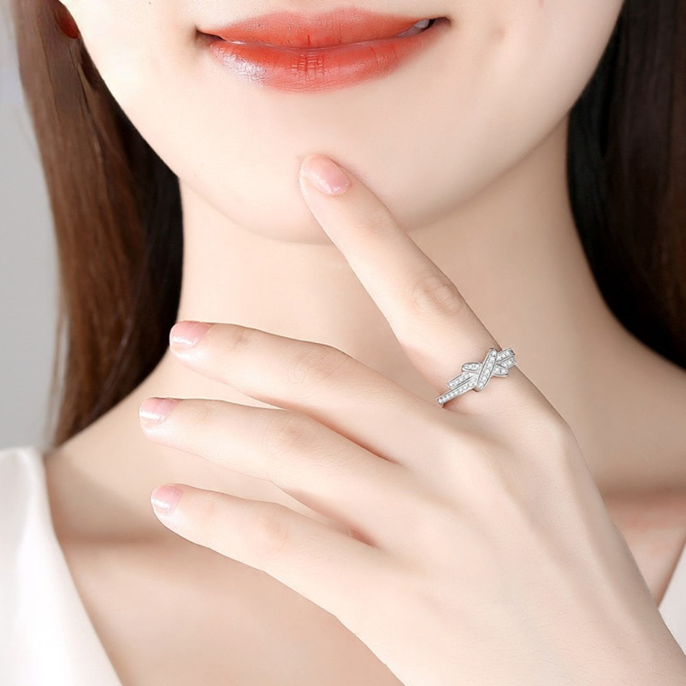 A hand wearing a silver pave bypass ring with a X studded with sparkling moissanites.
