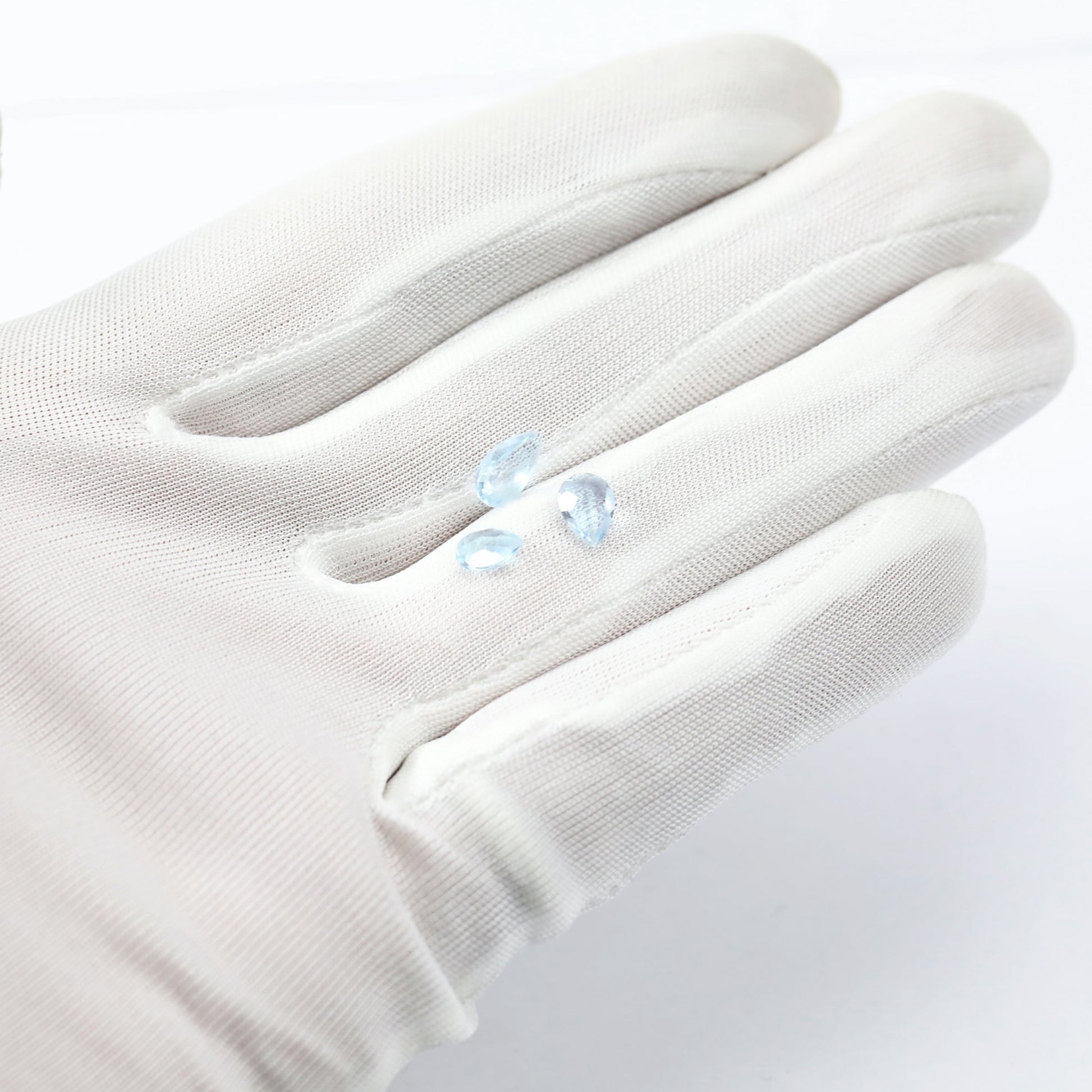 A hand holding 3 tear drop cut light blue aquamarine gems.