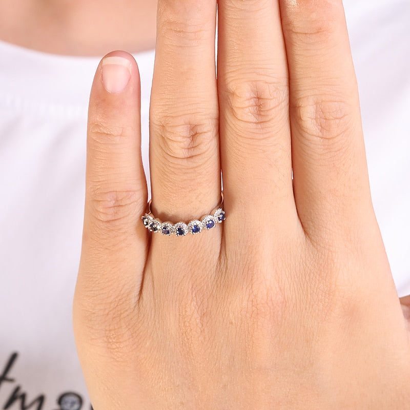 A hand wearing a silver wedding ring with 7 small lab grown sapphire encircled with moissanite halos.