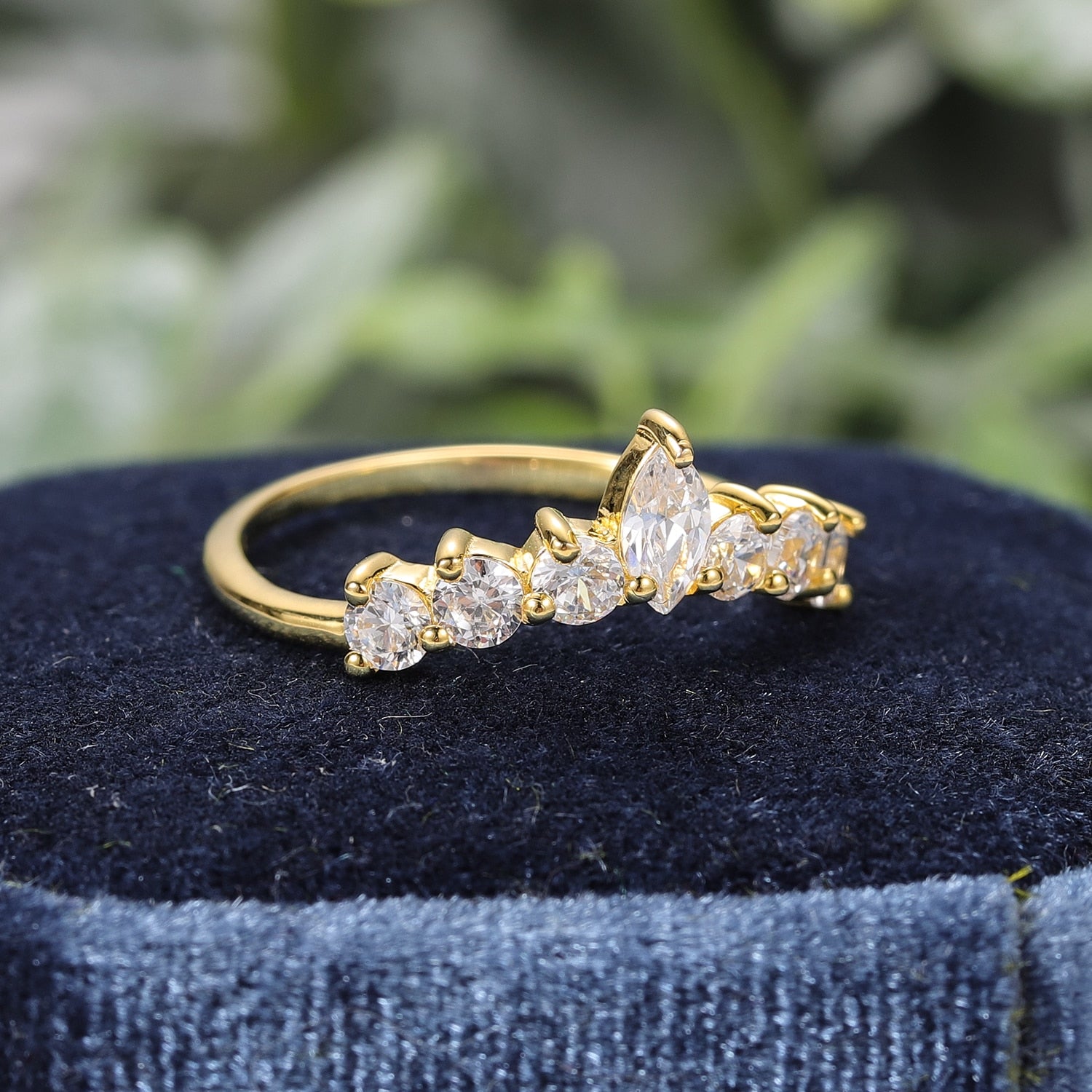 A gold slightly curved wedding ring with small round moissanites and a marquise moissanite in the center.