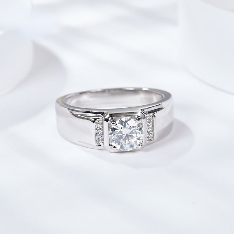 A silver thick banded ring set with a raised round moissanite and 4 sparkling gems on either side.