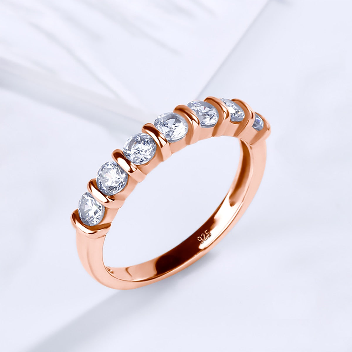 A rose gold band bar tension set with seven small moissanites.