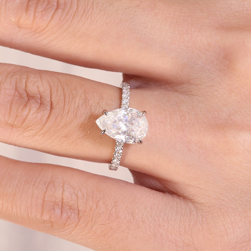 A hand wearing a silver 2.5CT oval cut moissanite ring with a hidden halo.