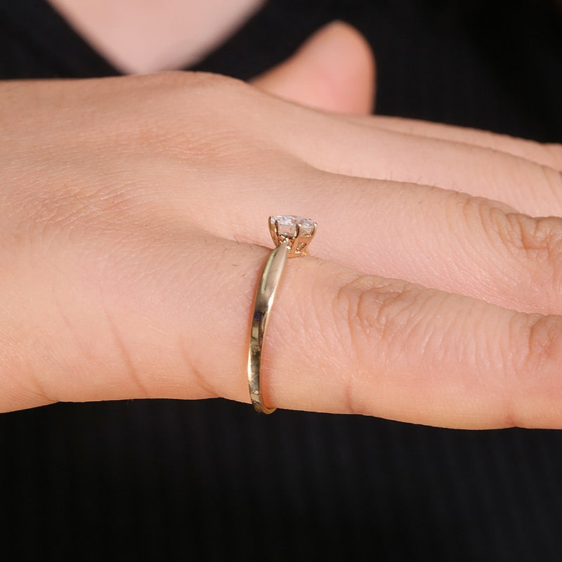 A hand wearing a gold small round solitaire with a tapered band.
