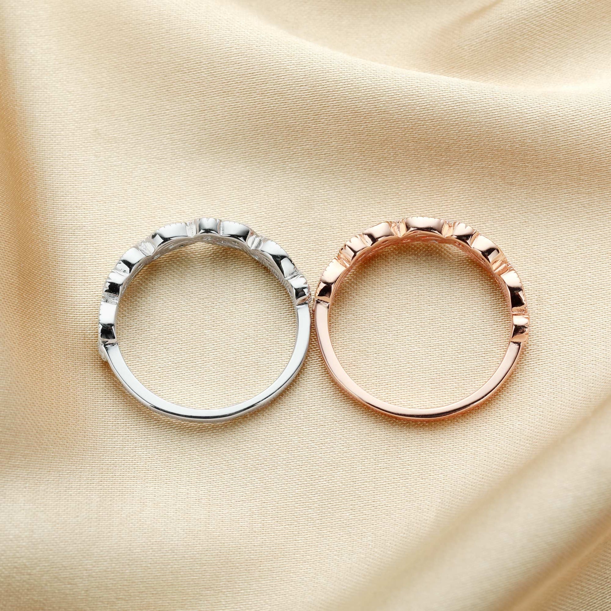 One silver and one rose gold swirl and leaf designed bands set with clear small gems.