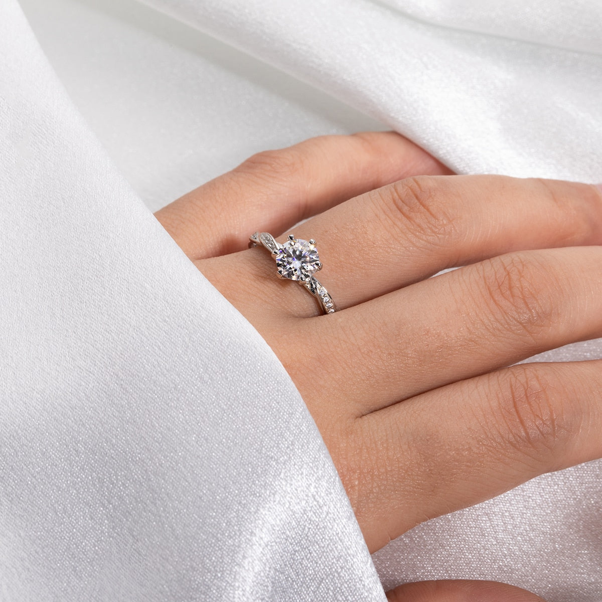 A hand wearing a silver ring with a twisted pave band and set with a round 1CT moissanite.