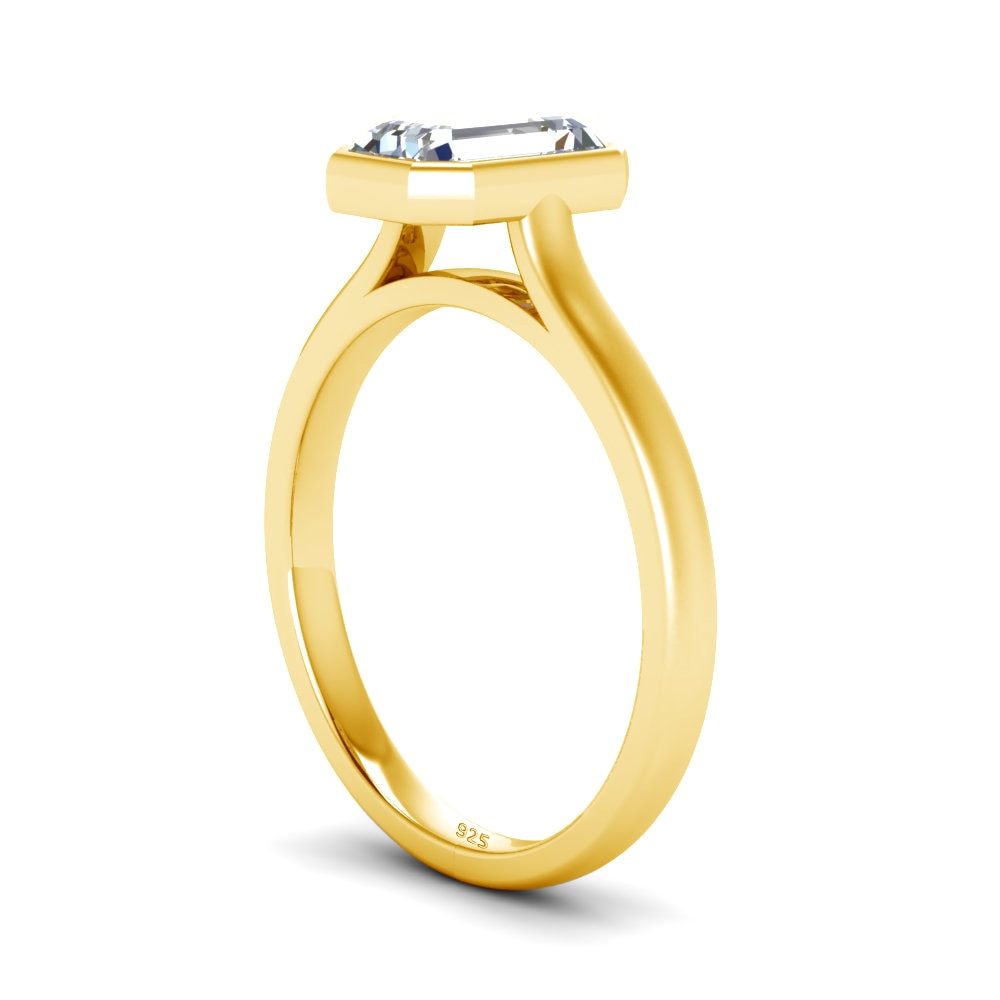 A gold bezel set emerald cut moissanite ring.