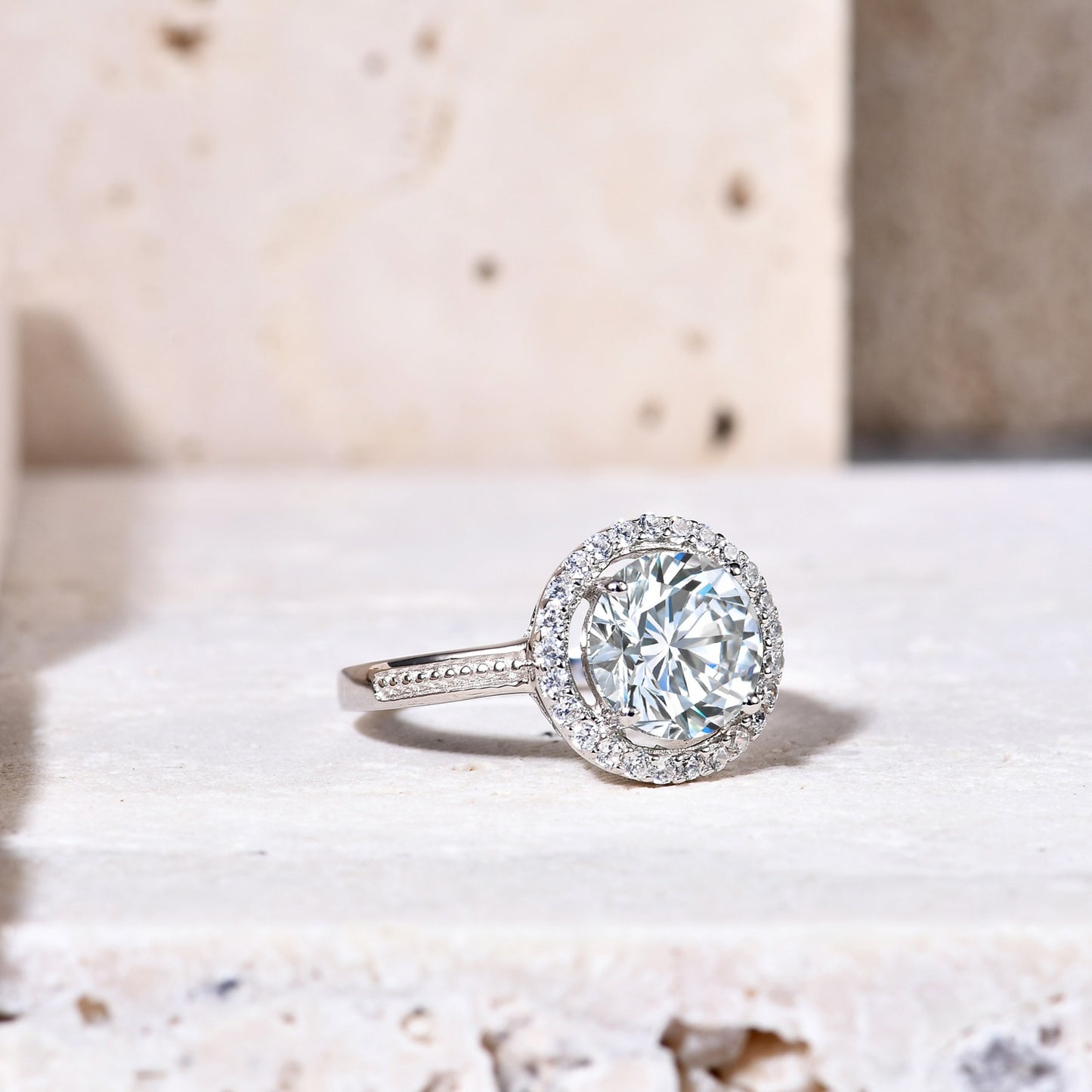 A silver halo ring set with a 2CT round moissanite encircled by a clear gem halo and set on a textured band.
