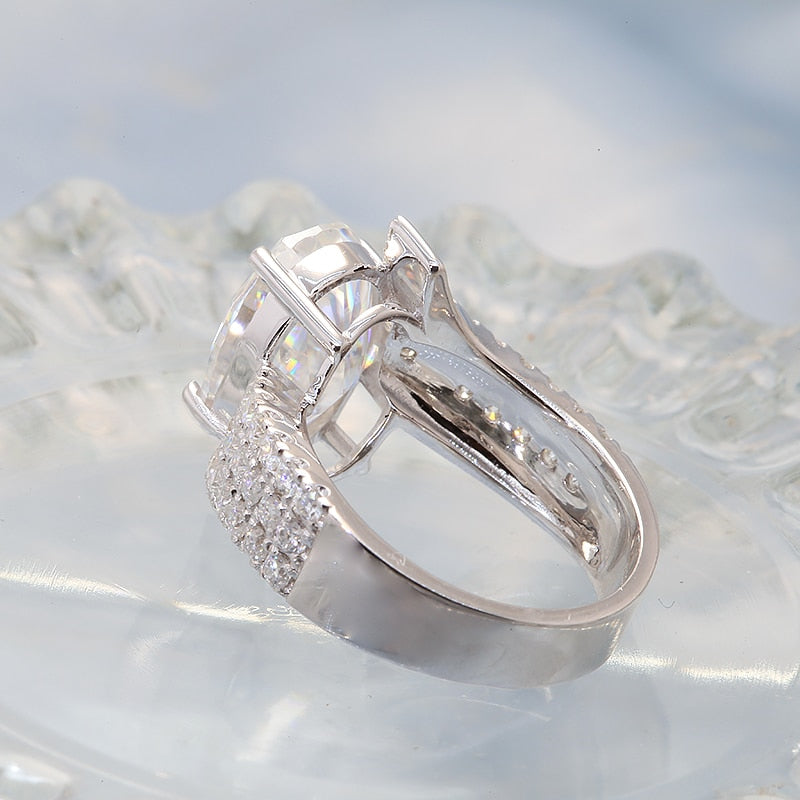 A silver ring set with a oval 6CT moissanite set in a triple row half pave bypass style band.