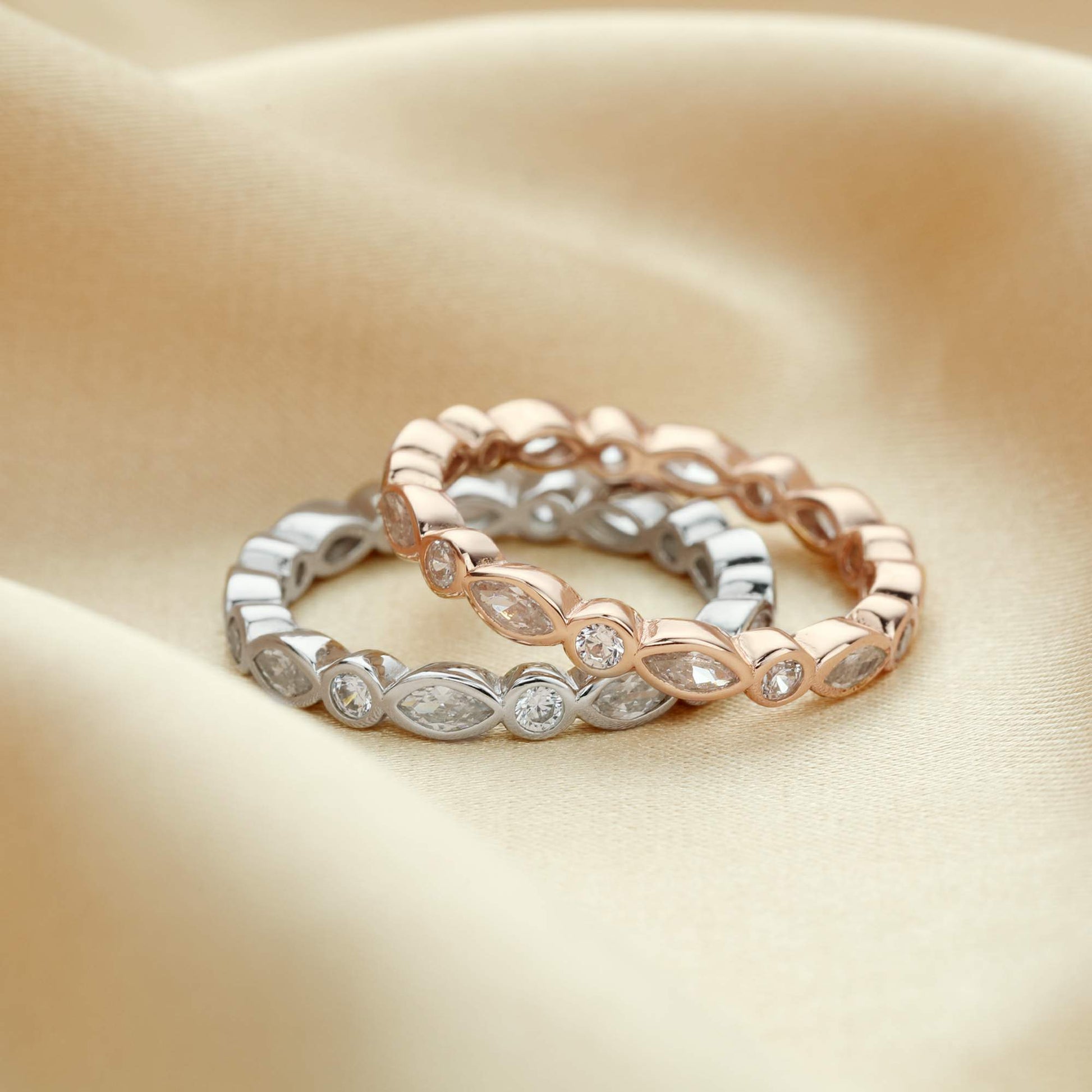One silver and one rose gold ring bezel set with alternating marquise and round cut clear gems.
