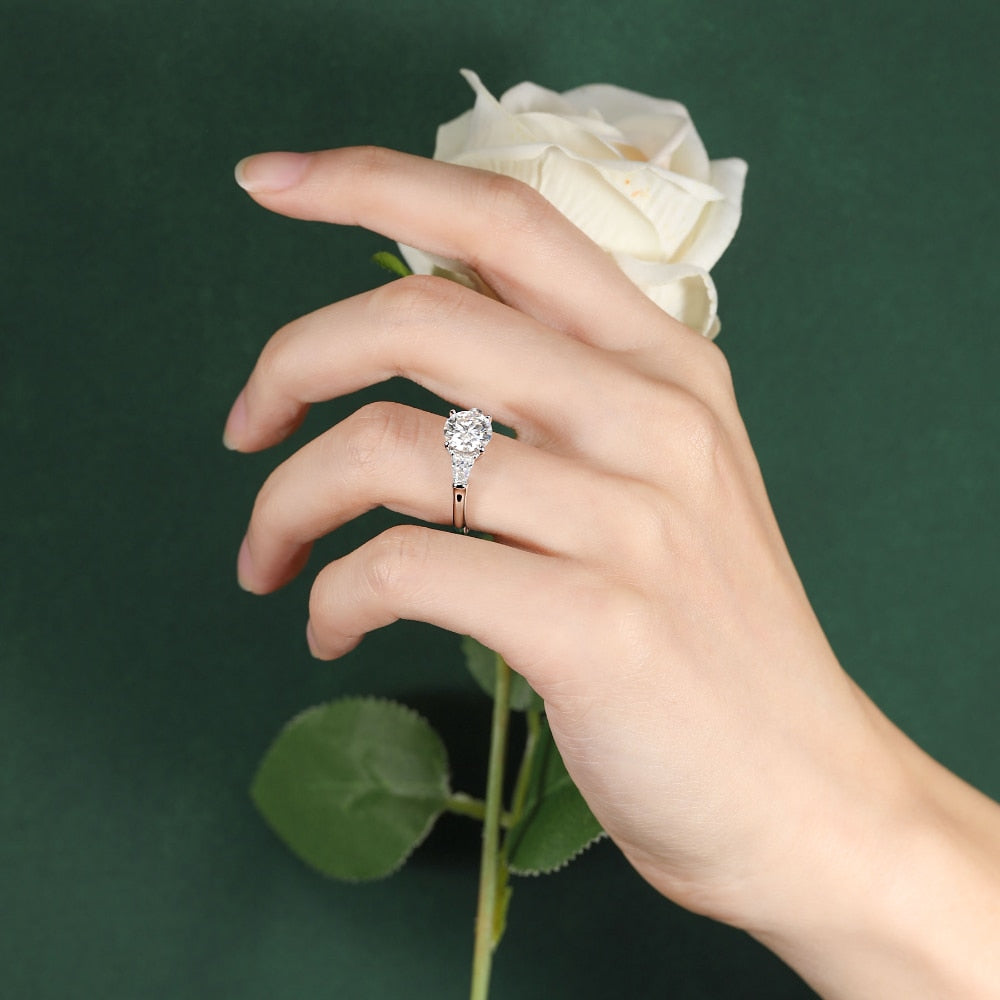 A hand wearing a silver round and trapezoid 3 stone engagement ring.