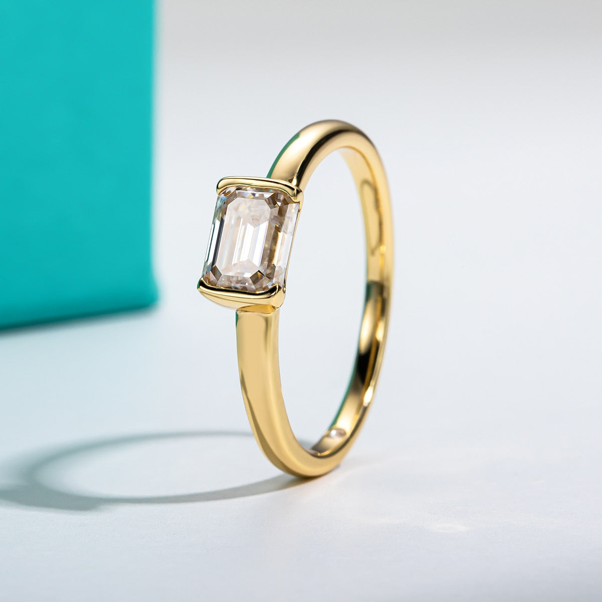 A gold tone ring set with a emerald cut moissanite set east to west in a tension bar setting.