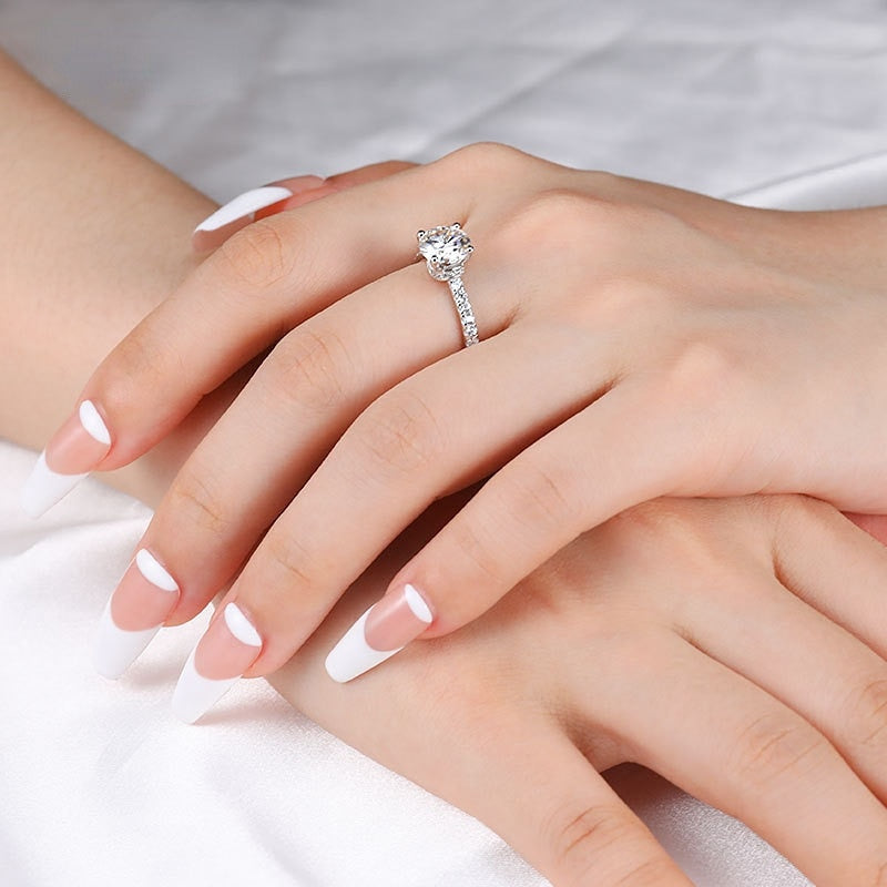 A hand wearing a silver round cut ring with V embellished necks and pave band.