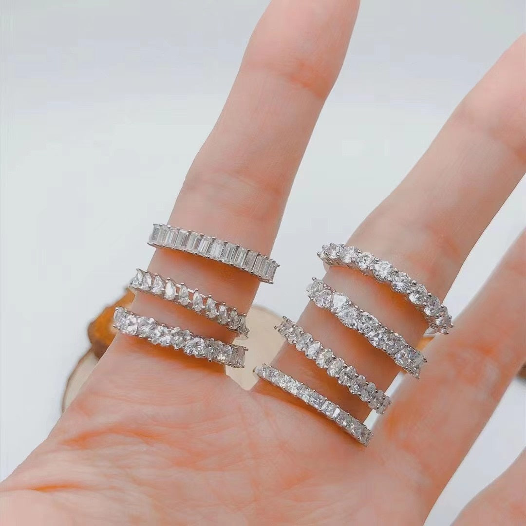 A hand wearing half eternity rings with various cuts of moissanite.