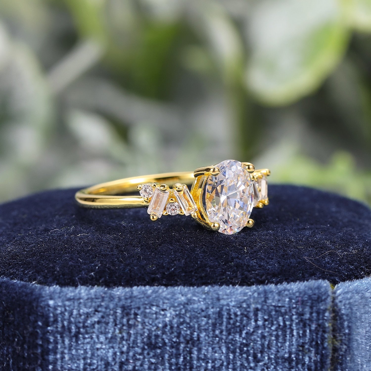 A gold ring set with a oval moissanite and 4 alternating emerald and round clear gems on either side.