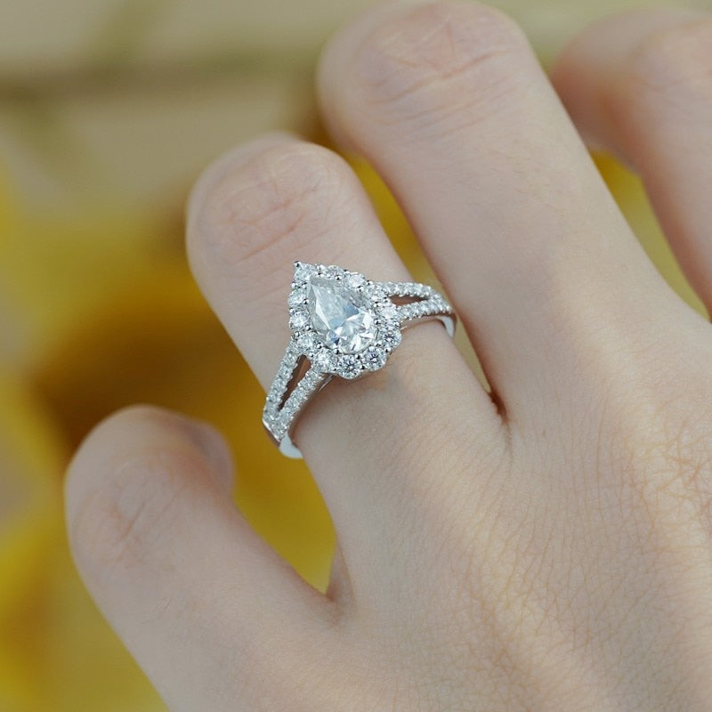 A hand wearing a silver tear drop halo split shank engagement ring.