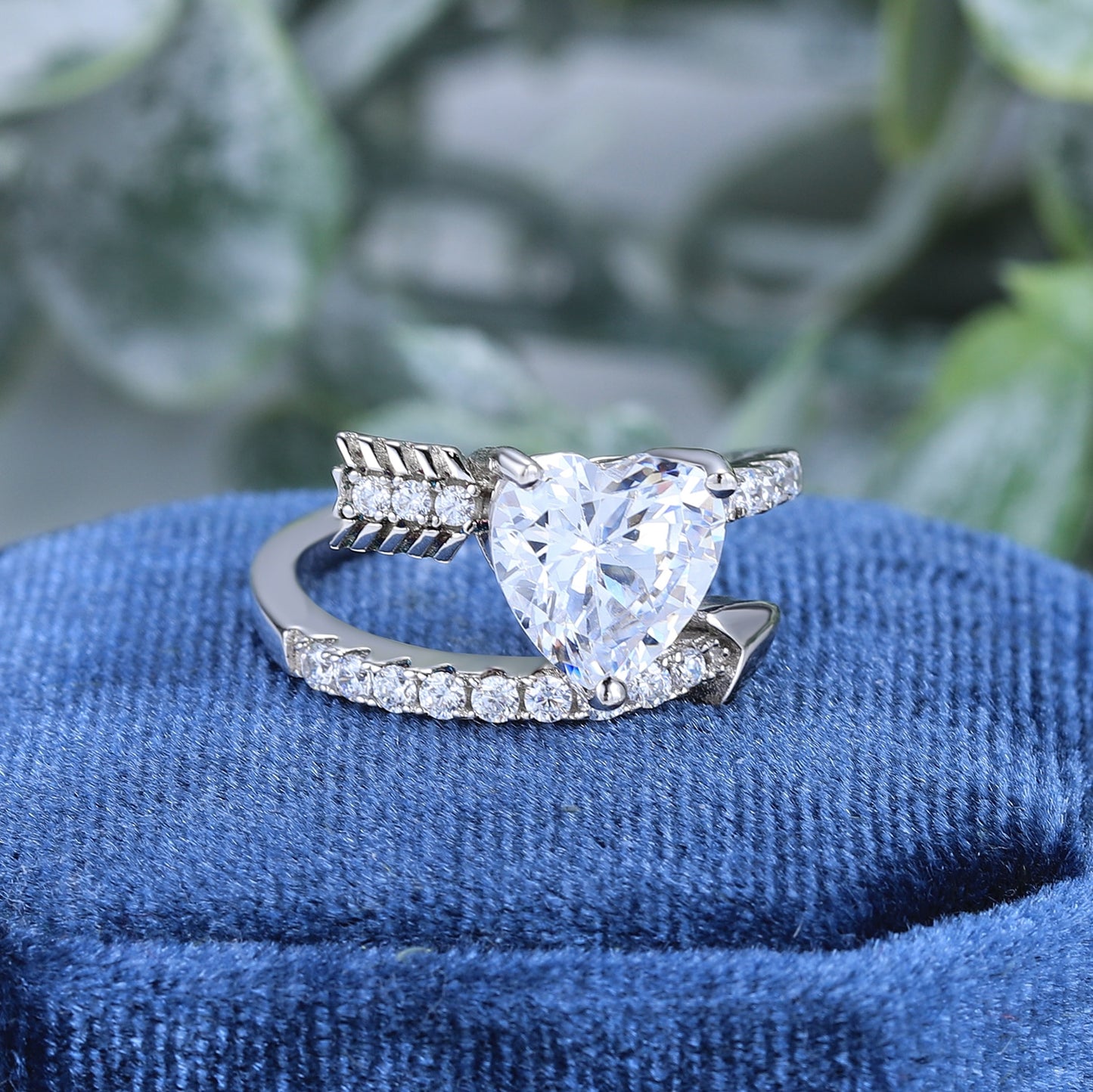 A silver wrap around bypass style ring resembling a pave studded arrow, set with a 4CT heart cut moissanite.