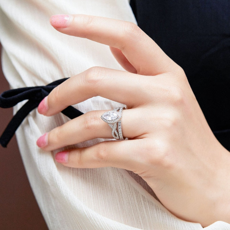 A hand wearing a silver engagement and wedding ring set with a marquise halo twisted band and eternity ring.