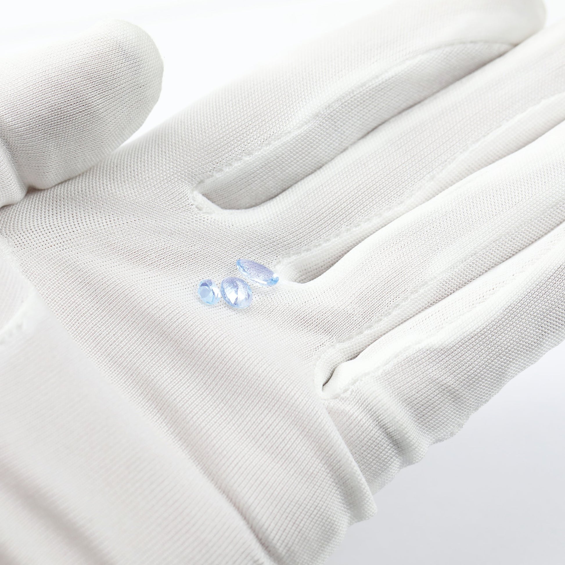 A hand holding 3 light blue oval aquamarine gems.