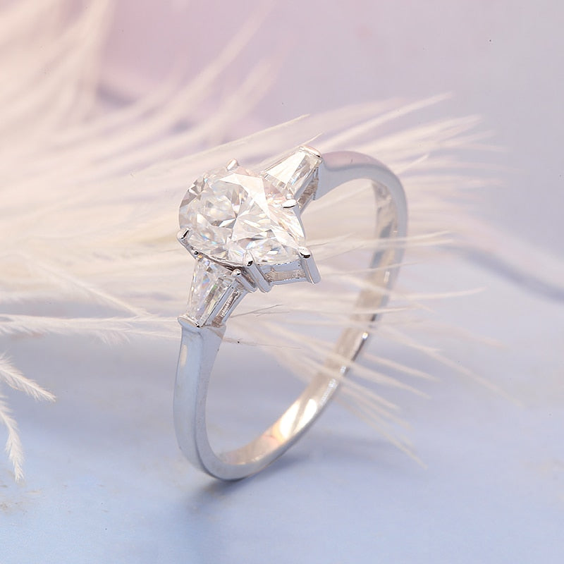 A silver 3 stone ring set with a 1.5CT pear cut moissanite set between two smaller baguettes.