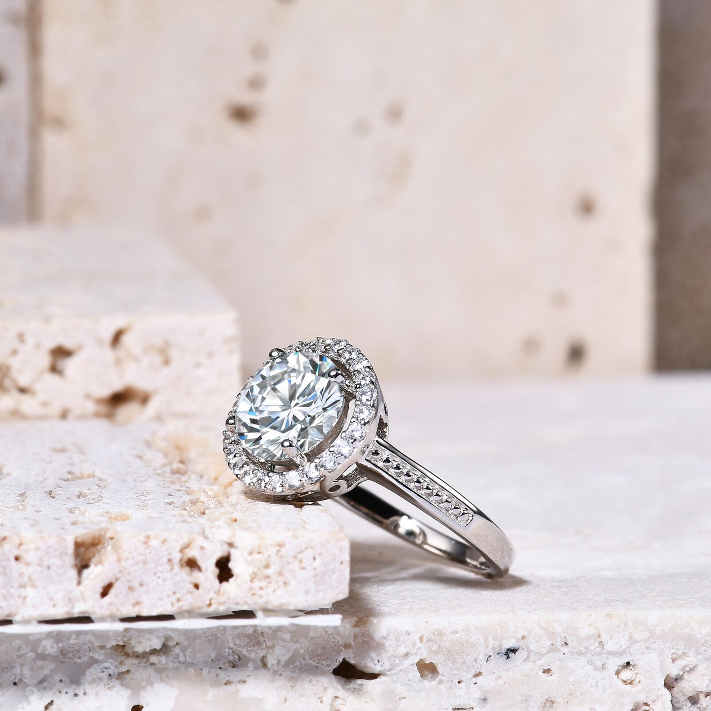 A silver halo ring set with a 2CT round moissanite encircled by a clear gem halo and set on a textured band.