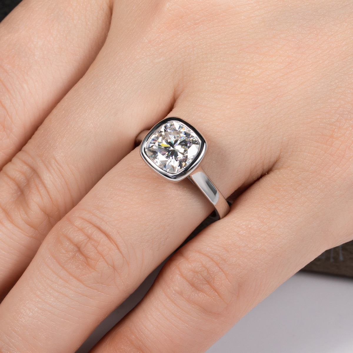 Hand wearing a sterling silver ring with a 3CT cushion cut moissanite gem bezel set.