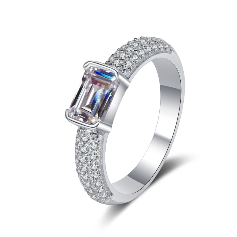 A silver gem encrusted band with a emerald cut moissanite tension set, east to west.
