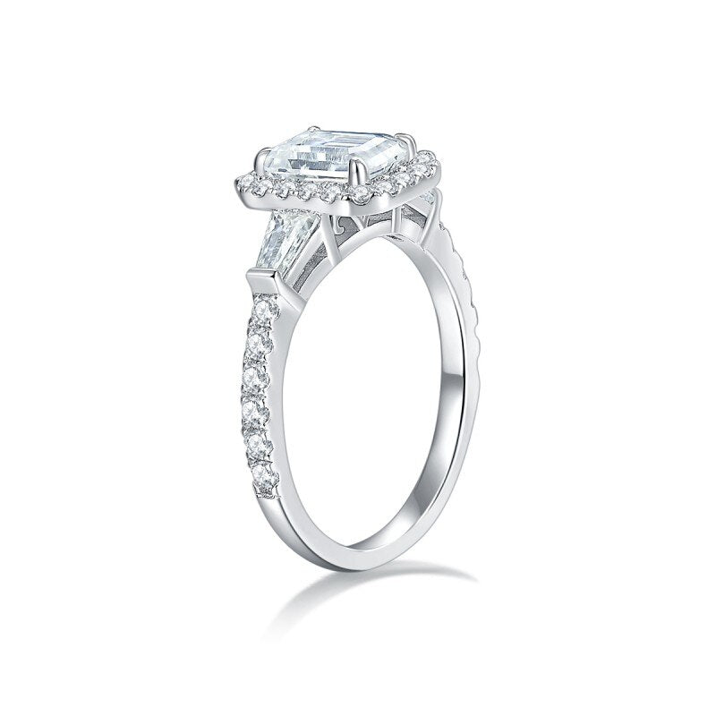 A silver engagement ring set with an emerald cut moissanite and is a hybrid 3 stone halo style.
