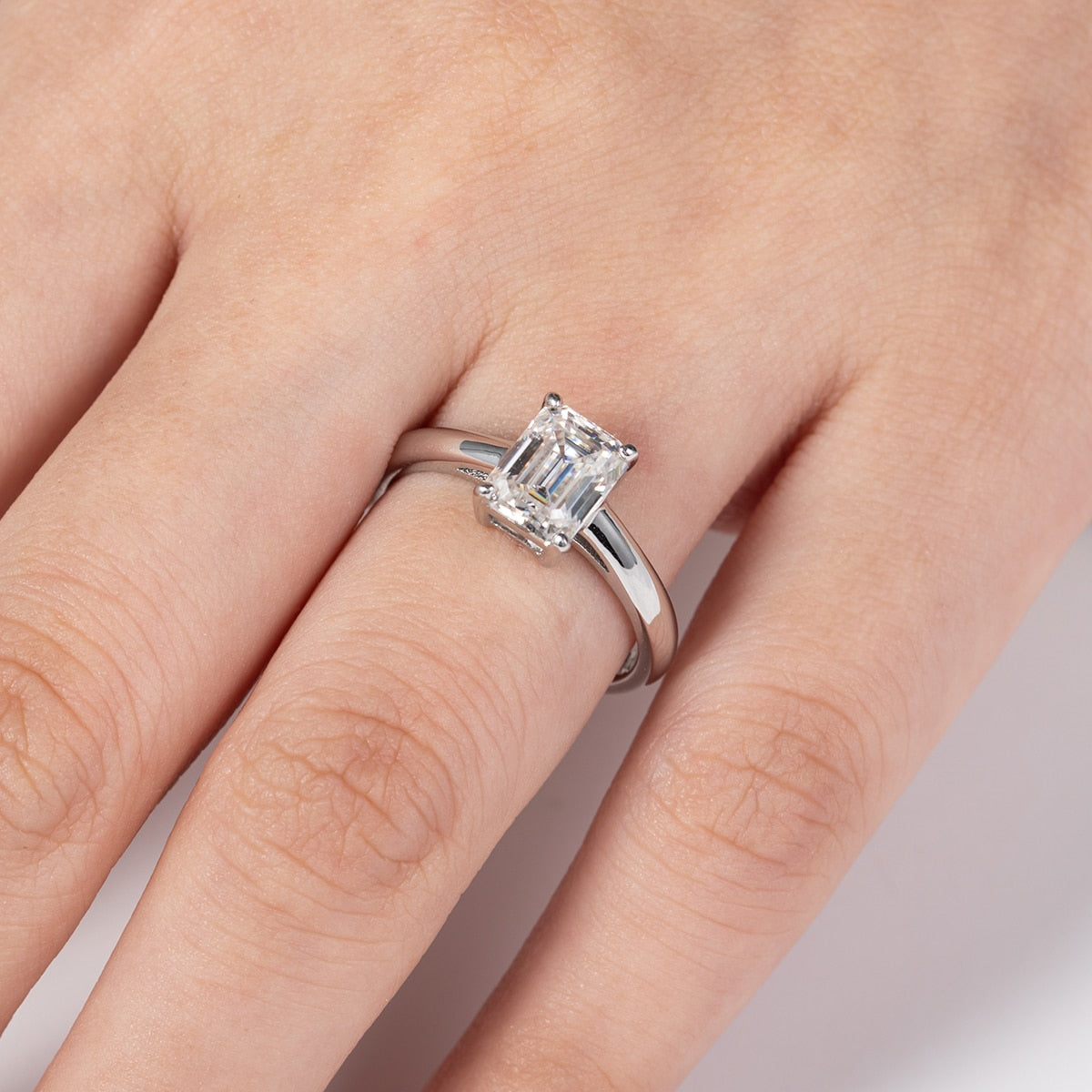 A Hand wearing a 2CT emerald cut moissanite sterling silver ring.