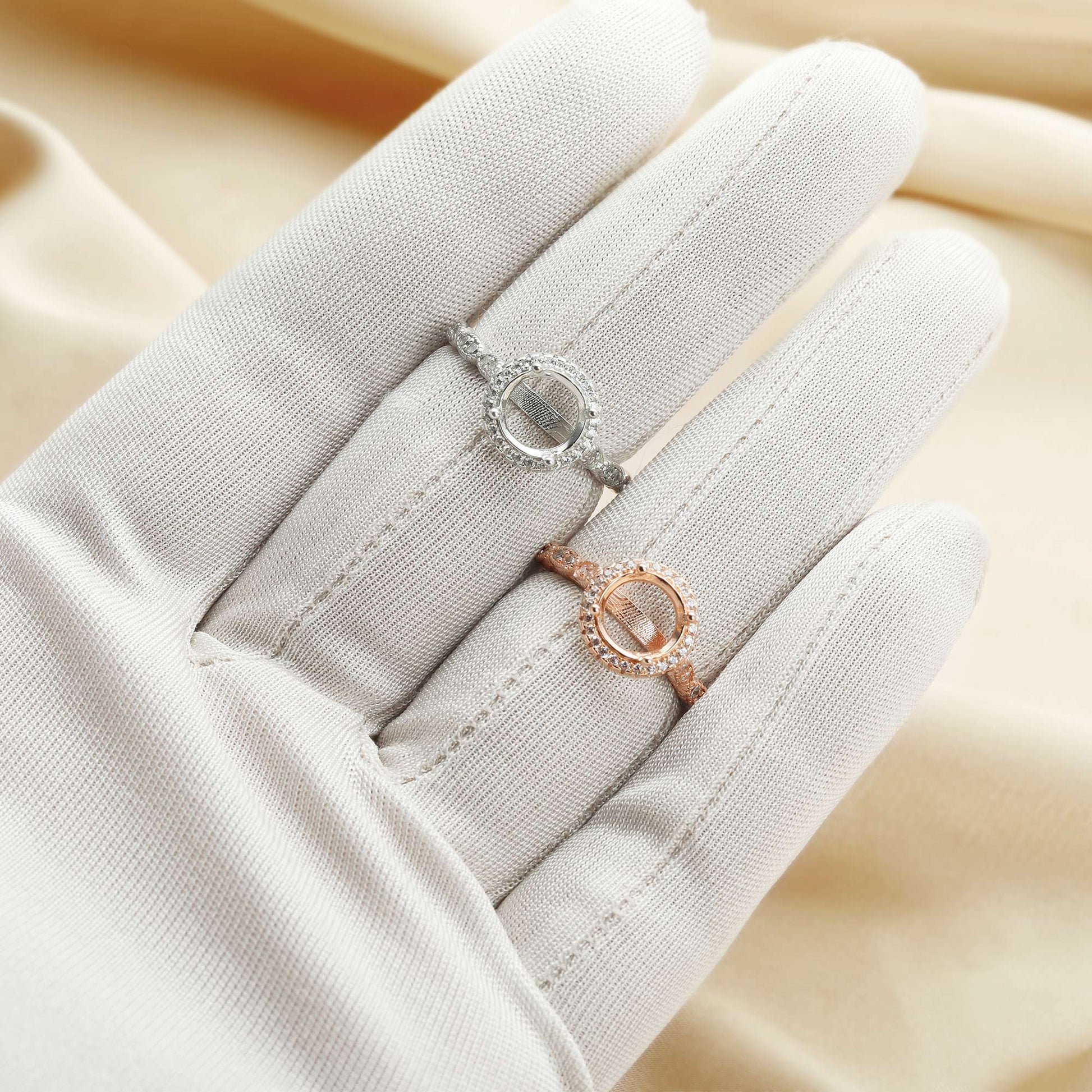 A silver round halo art deco style semi mount and a identical rose gold semi mount worn on a hand.