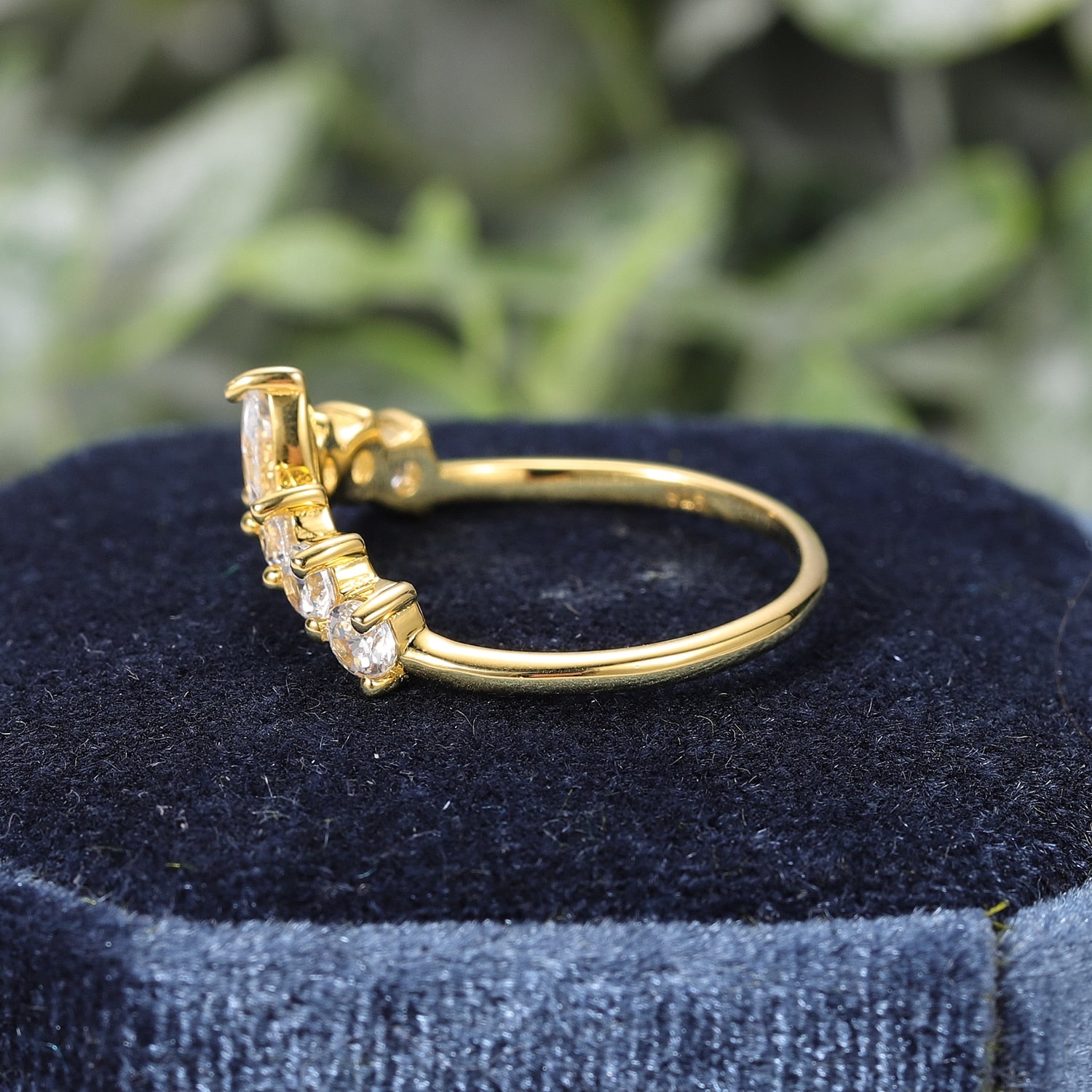 A gold slightly curved wedding ring with small round moissanites and a marquise moissanite in the center.