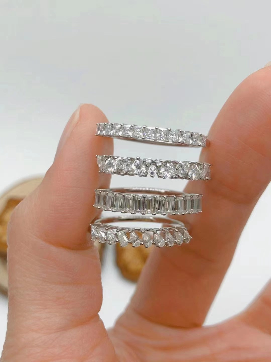 A hand holding 4 silver wedding rings set with several small princess, heart, tear drop and emerald cut moissanites.