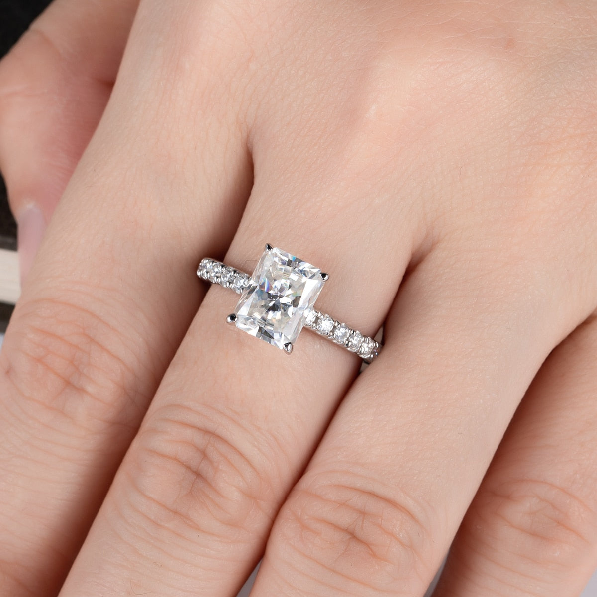 A hand wearing a moissanite ring with a 3CT radiant cut gem set on a moissanite pave band.