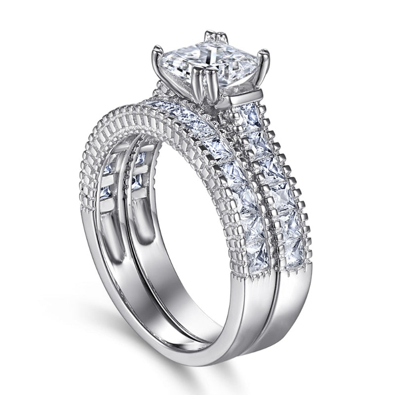 A silver engagement ring set with a princess cut moissanite on a princess cut pave style shank with a matching wedding band.