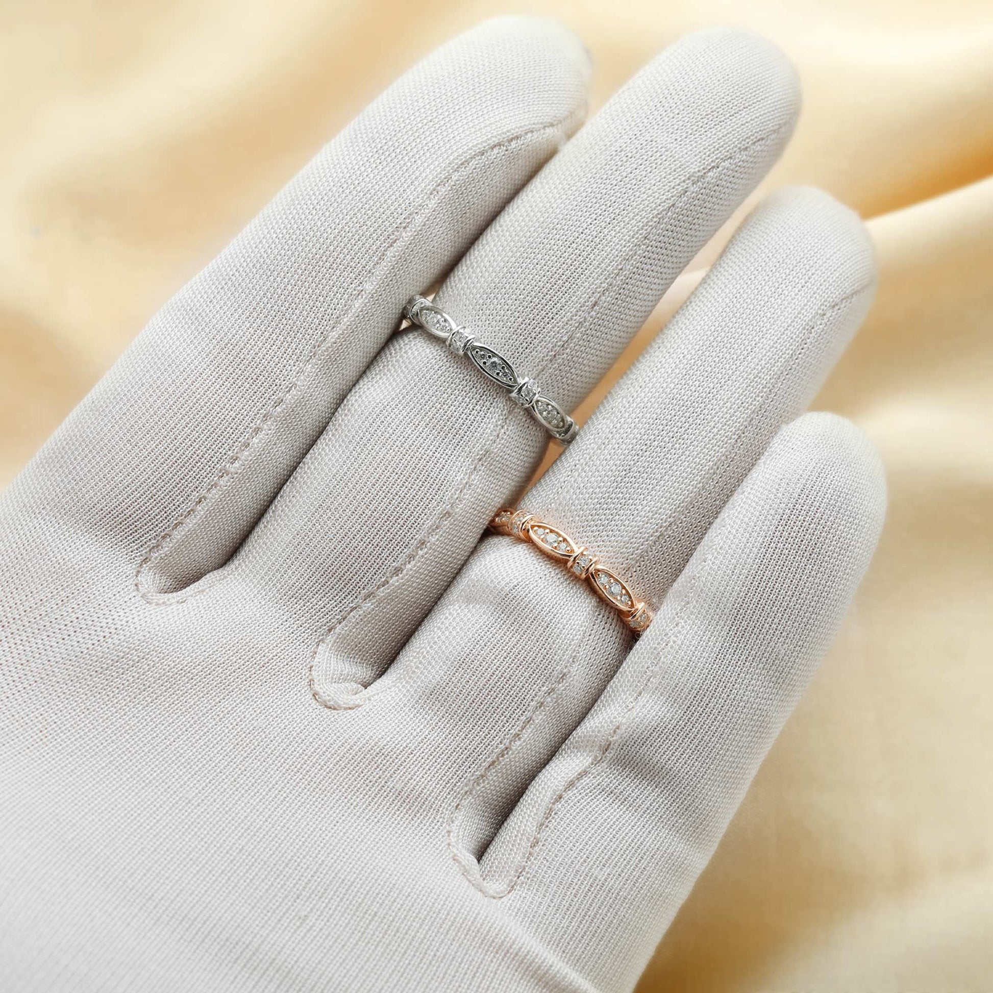 A hand wearing one silver and one rose gold ribbon scalloped style ring set with clear small gems.