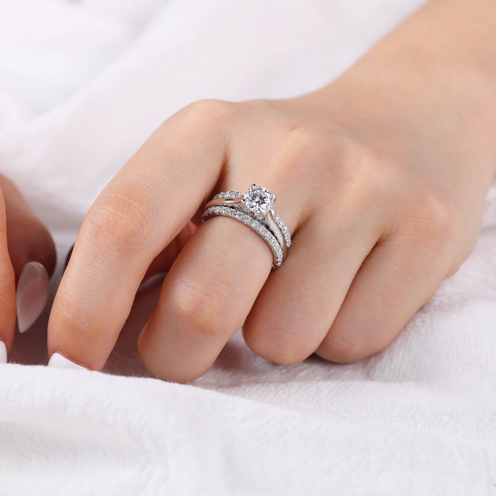 A  hand wearing a silver bridge embellished cathedral set round engagement ring.